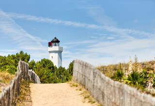 Sandy path with wooden fence leading to lighthouse surrounded by trees near La Tranche-sur-Mer, Pays de la Loire, France.