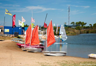 Boats with orange sails on shore at Flower Camping l'Escale du Perthuis, Pays de la Loire, France.