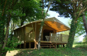 Tenda safari con veranda in legno e sedie di plastica, immersa in una zona boschiva ricca di verde.