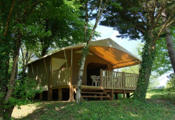 Tenda safari con veranda in legno e sedie di plastica, immersa in una zona boschiva ricca di verde.