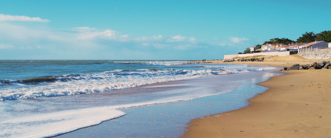 Grande plage de sable avec vagues et maisons côtières à Flower Camping l'Escale du Perthuis, Pays de la Loire.