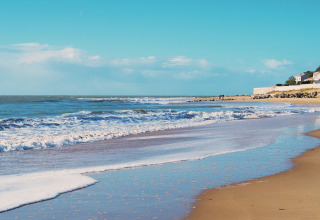 Wide sandy beach with ocean waves and coastal houses at Flower Camping l'Escale du Perthuis, Pays de la Loire.