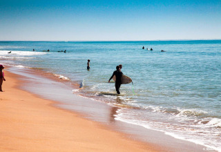 Surfer verlaat de zee bij Flower Camping l'Escale du Perthuis in Pays de la Loire met mensen op het strand.