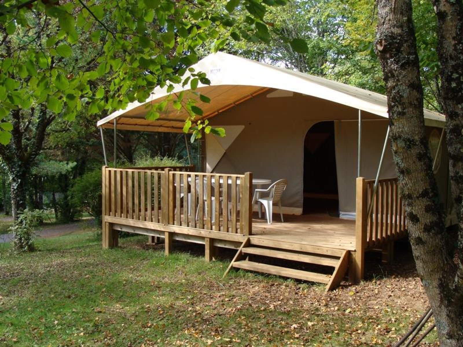 Safari tent Lodge Canada Classic met houten veranda en tuinmeubilair, omringd door groene bomen.