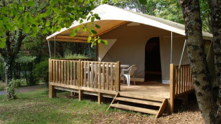 Safari tent Lodge Canada Classic with wooden deck and outdoor chairs, nestled in a leafy, green forest setting.