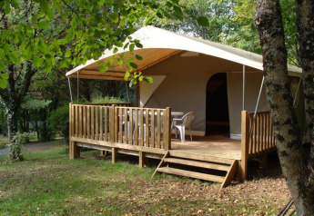 Tienda safari Lodge Canada Classic con terraza de madera y sillas, rodeada de árboles y naturaleza verde.