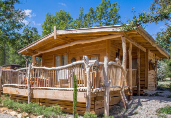 A rustic wooden chalet lodge with a porch, set amongst trees and greenery under a bright blue sky.
