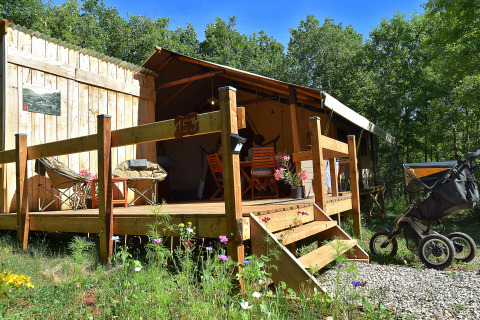 Safaritent met eigen terras en sanitair, midden in de natuur, kinderwagen voor het terras geparkeerd.