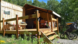 Tienda safari con terraza privada y baños, rodeada de naturaleza, con cochecito en primer plano.