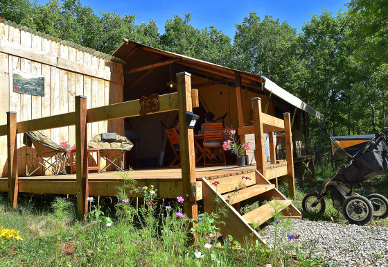 Safaritent met eigen terras en sanitair, midden in de natuur, kinderwagen voor het terras geparkeerd.