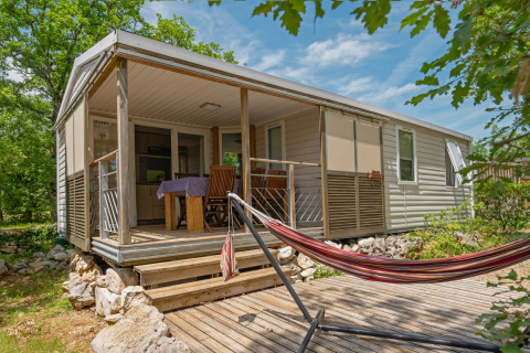 Mobilheim Midi Pyrénées mit überdachter Terrasse, Esstisch, Stühlen und Hängematte auf Holzdeck.