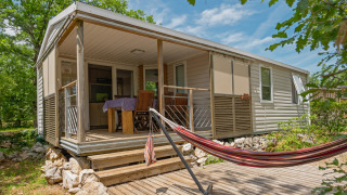 Mobil-home en Midi Pyrénées avec terrasse couverte, table à manger, chaises et hamac sur terrasse.
