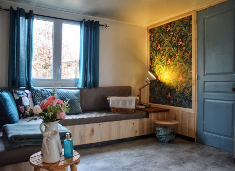 Acogedor rincón en la Upupa lodge con cortinas azules, cojines florales y pared con papel decorativo.