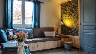 Accogliente angolo salotto nella lodge Upupa con tende blu, cuscini floreali e carta da parati vivace.