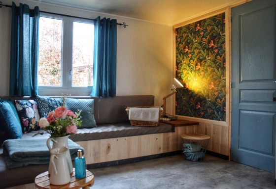 Acogedor rincón en la Upupa lodge con cortinas azules, cojines florales y pared con papel decorativo.