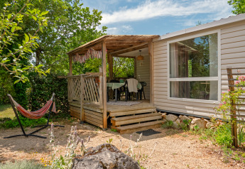Mobile home Loggia: Houten veranda met eettafel en hangmat, omgeven door groene en rustige natuur.