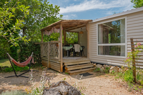 Mobile Home Loggia: Holzterrasse mit Esstisch und Hängematte inmitten grüner Vegetation und Ruhe.