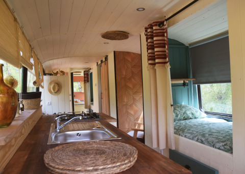 Interno della Lijn 3C, scuola bus lodge accogliente con cucina, letto matrimoniale e luce naturale.