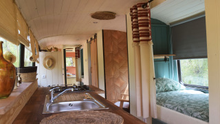 Interior of Lijn 3C cozy school bus lodge featuring kitchen, double bed, natural light, and decor.