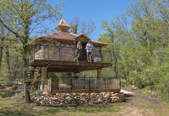 Due persone sul balcone della casa sull'albero Duiventoren, immersa in una fitta foresta verde.