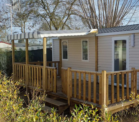 Casa mobile moderna con terrazza in legno, tenda da sole e giardino, situata vicino alla spiaggia e al sole.
