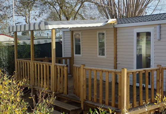 Mobil-home moderne avec terrasse en bois, auvent et jardin, situé près de la plage pour des vacances reposantes.