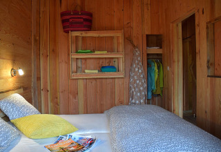 Bedroom interior at Chalet, Campsite Les 3 Cantons, France, featuring wooden walls, bed, and colorful linens.