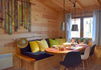 Cozy dining nook in a wooden chalet at Les 3 Cantons campsite, France, with colorful cushions and tableware.