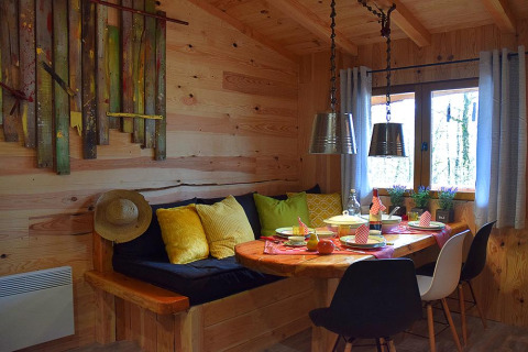 Accogliente angolo pranzo in chalet di legno al campeggio Les 3 Cantons, Francia, con cuscini e stoviglie colorati.