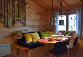 Accogliente angolo pranzo in chalet di legno al campeggio Les 3 Cantons, Francia, con cuscini e stoviglie colorati.