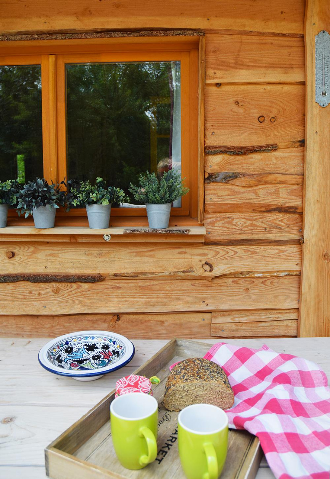 Buitentafel met brood, groene mokken, kleurrijk bord en plantjes bij Chalet op camping Les 3 Cantons in Frankrijk.