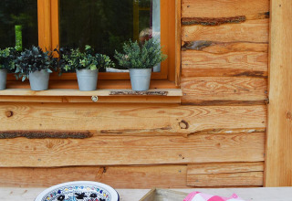 Tavolo rustico con pane, tazze verdi, piatto e piante davanti a finestra dello Chalet al campeggio Les 3 Cantons in Francia.