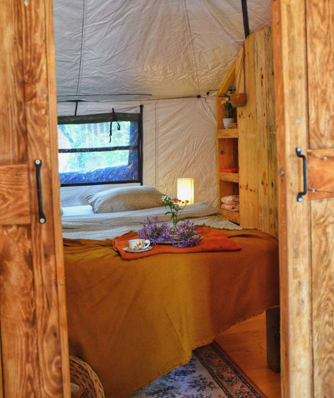 Sfeervol interieur van safaritent Dôme op Camping Les 3 Cantons in Frankrijk met bed en houten meubels.