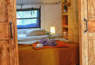 Interno accogliente della tenda safari Dôme al campeggio Les 3 Cantons in Francia, con letto e mobili in legno.