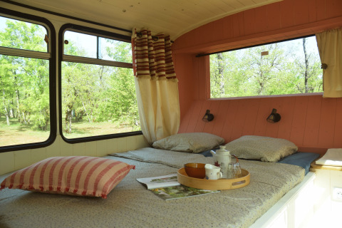 Interno di un accogliente lodge-scuolabus con letto, grandi finestre e vista verde a Les 3 Cantons.