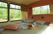 Interno di un accogliente lodge-scuolabus con letto, grandi finestre e vista verde a Les 3 Cantons.