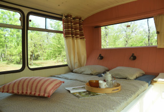 Interno di un accogliente lodge-scuolabus con letto, grandi finestre e vista verde a Les 3 Cantons.