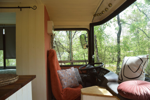 Gemütlicher Innenraum eines Schulbus-Lodges mit Kissen und großem Fenster im Les 3 Cantons Campingplatz, Frankreich.