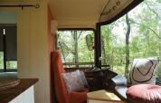 Interno accogliente di lodge bus scolastico con cuscini e vista sugli alberi a Les 3 Cantons, Francia.