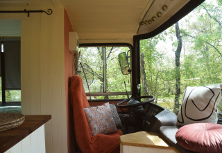 Interno accogliente di lodge bus scolastico con cuscini e vista sugli alberi a Les 3 Cantons, Francia.