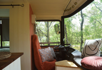 Interno accogliente di lodge bus scolastico con cuscini e vista sugli alberi a Les 3 Cantons, Francia.