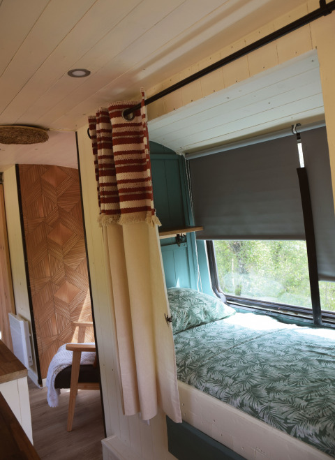 Innenraum der Lijn 3C cozy school bus Lodge auf dem Campingplatz Les 3 Cantons in Frankreich mit Bett und Vorhängen.