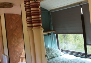 Innenraum der Lijn 3C cozy school bus Lodge auf dem Campingplatz Les 3 Cantons in Frankreich mit Bett und Vorhängen.
