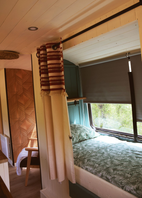 Interno del Lijn 3C cozy school bus al campeggio Les 3 Cantons in Francia, con letto e tende.