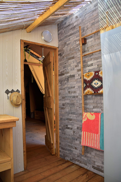 Interieurfoto van safaritent op Camping Les 3 Cantons in Frankrijk met houten vloer en stenen muur.