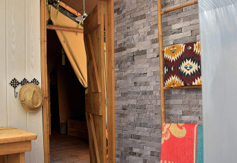 Vista interior de una tienda safari en el camping Les 3 Cantons, Francia, con decoración de madera y piedra.