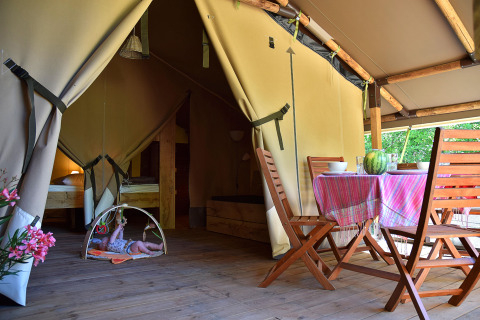 Binnenaanzicht van een safaritent op Camping Les 3 Cantons in Frankrijk, met eethoek en een baby.