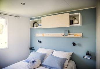 Camera moderna con parete blu, biancheria bianca e scaffali allo Starcaravan Lavaurette, Les 3 Cantons.