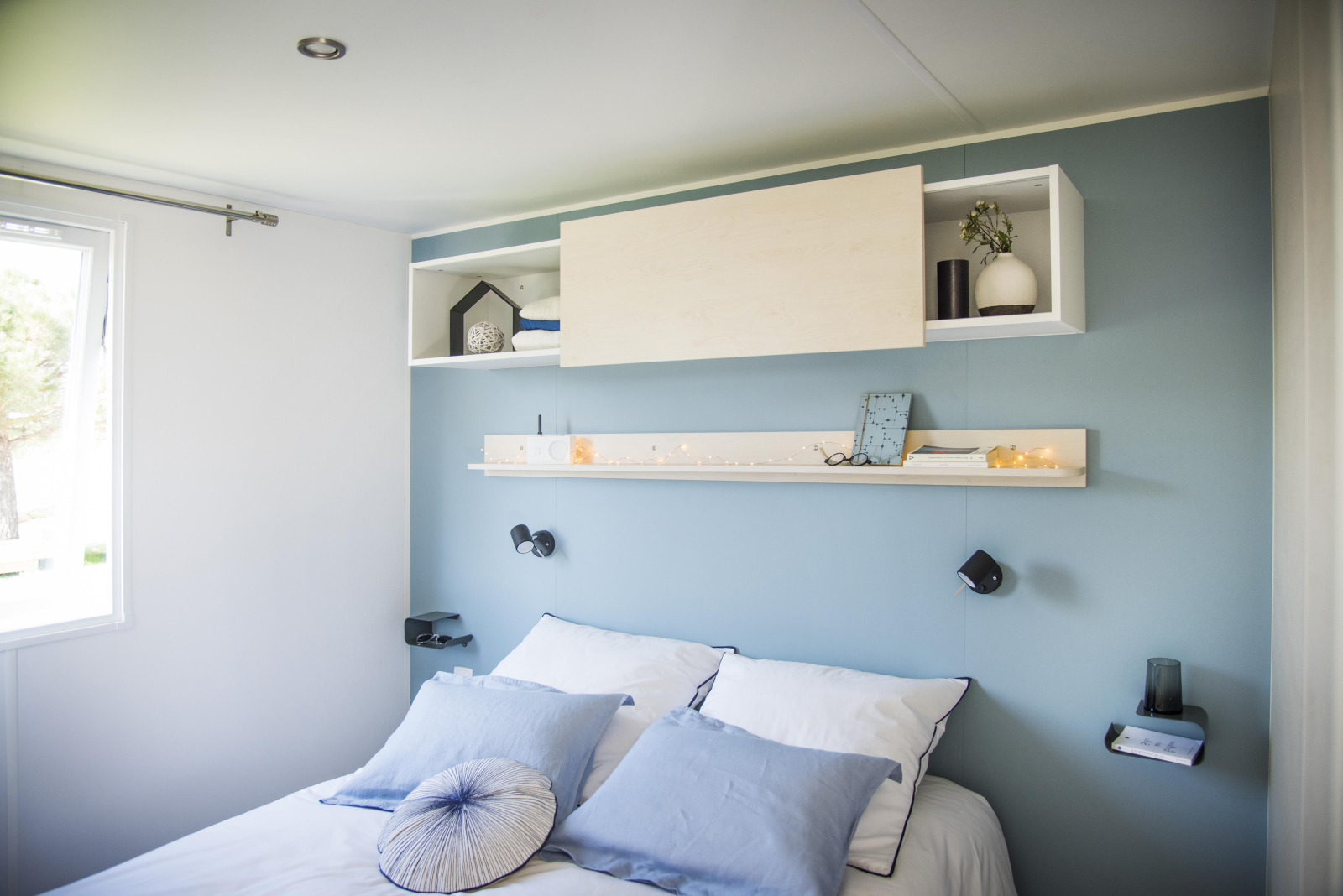 Moderne slaapkamer met blauwe muur, wit beddengoed en planken bij Starcaravan Lavaurette, Les 3 Cantons.
