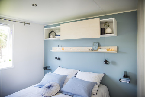 Chambre moderne avec mur bleu, literie blanche et étagères au Starcaravan Lavaurette, Les 3 Cantons.